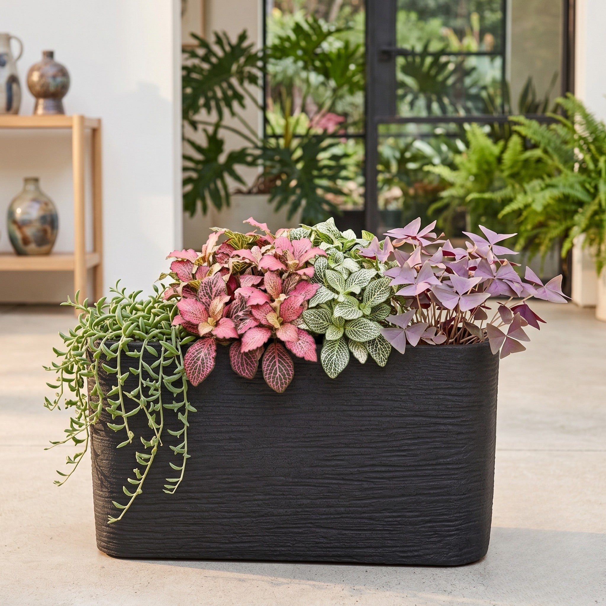 Nora 26-inch rectangular planter in black with a textured stone finish, filled with vibrant indoor plants.