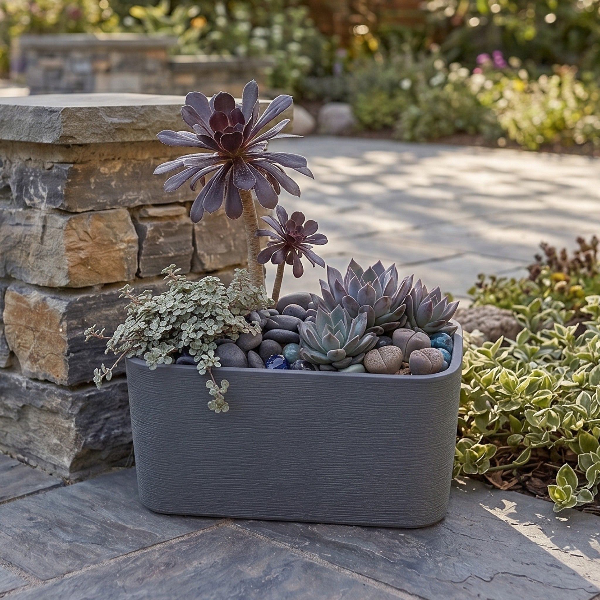 Nora 26-inch grey rectangular planter with a textured finish, filled with assorted succulents on a stone patio.