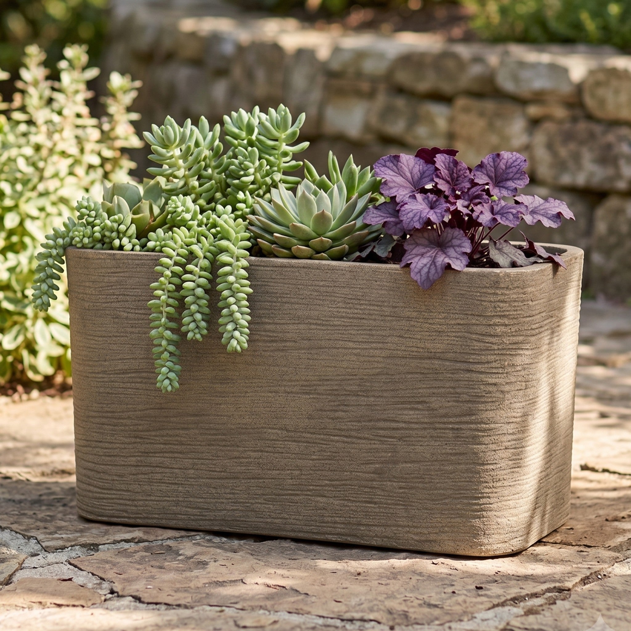 Nora 26-inch rectangular planter with a textured stone finish, filled with various succulents on a stone patio.