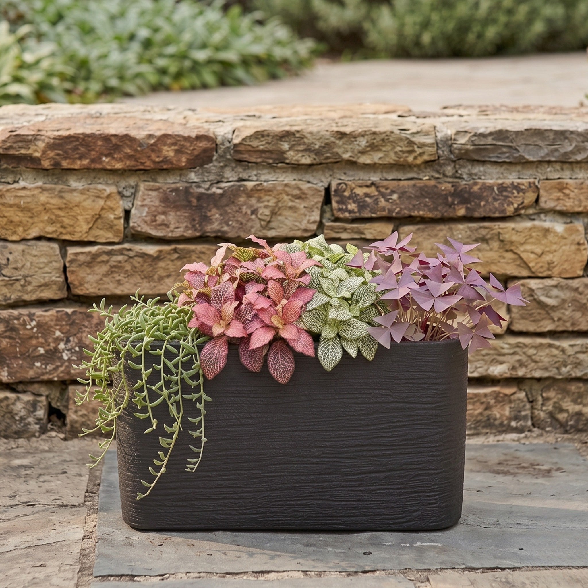Nora 26-inch rectangular planter in dark textured polymer filled with a variety of colorful indoor plants