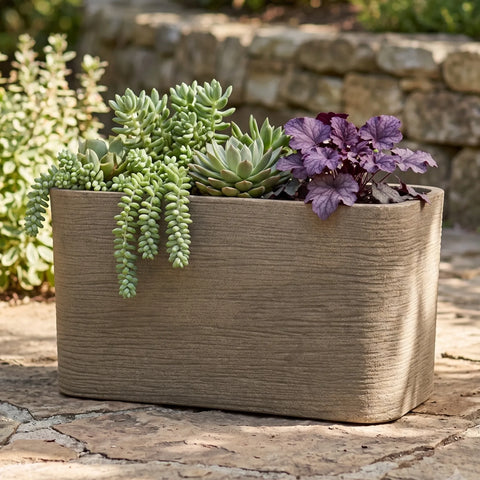 Nora 26-inch rectangle planter with a textured stone finish, holding a variety of succulents on a stone patio.